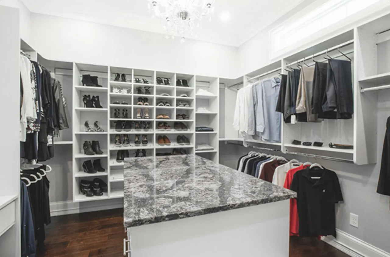 White walk-in closet with a granite-topped center island, a wall of shoe cubbies and double hanging under a chandelier