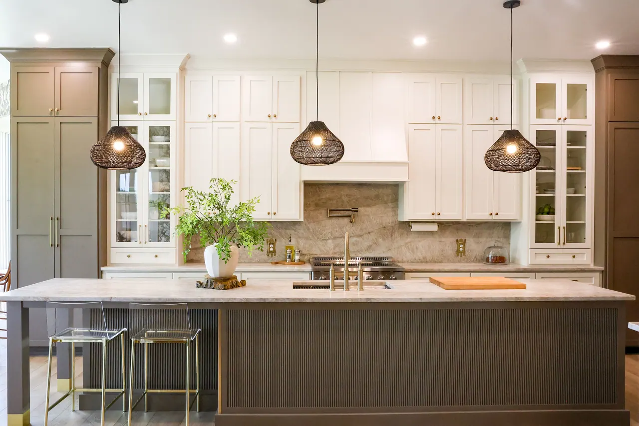Two-tone kitchen with gray-green island and white upper cabinets under pendant lights