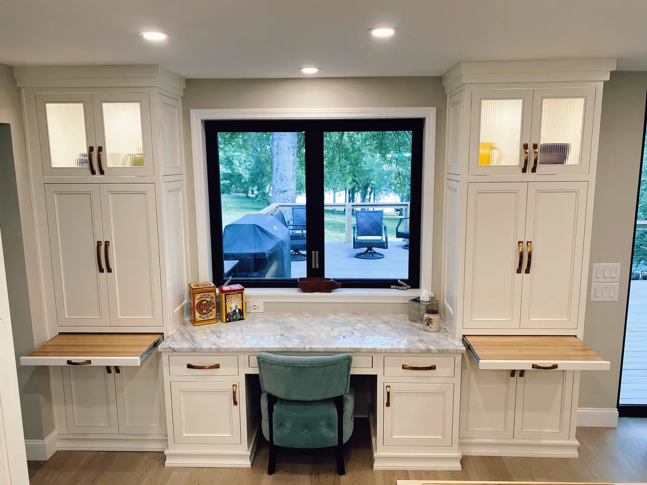 Built-in white desk nook under a window with glass-front uppers