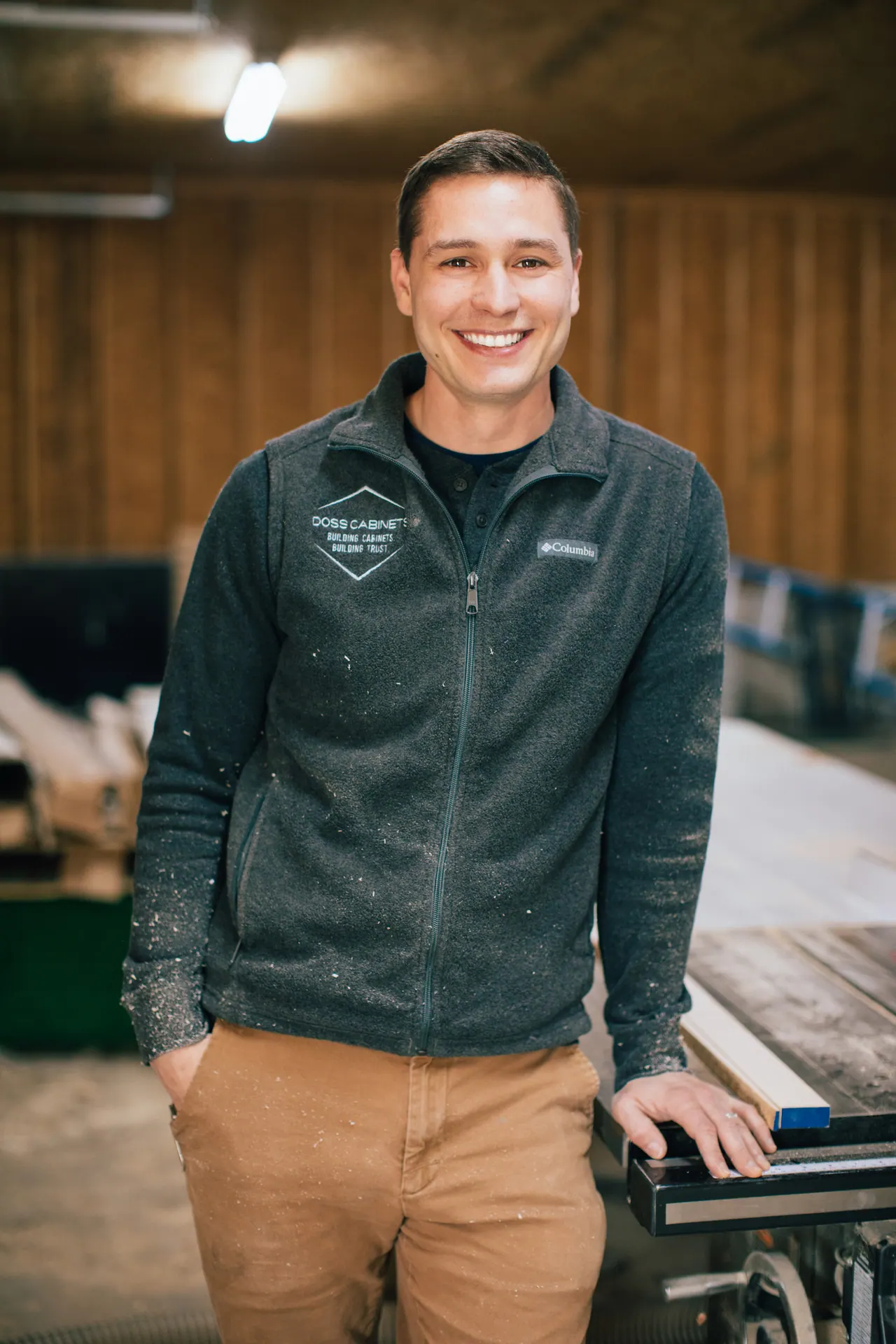 Clayton Doss smiling beside the table saw in the Doss Cabinets shop