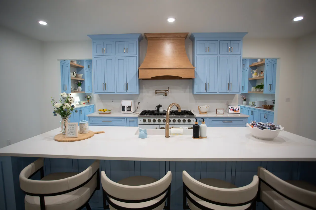 Wide view of a blue painted kitchen with a wood range hood, open shelves and island seating