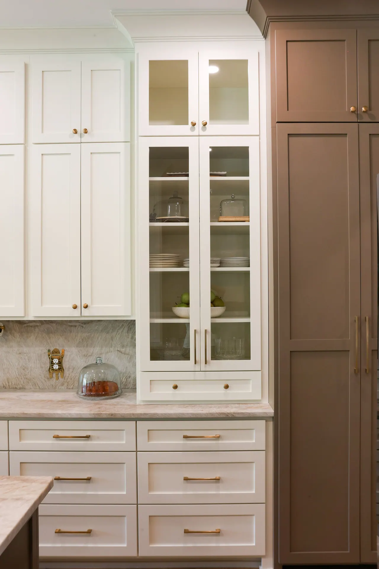 Glass-front white display cabinet beside a tall stained pantry